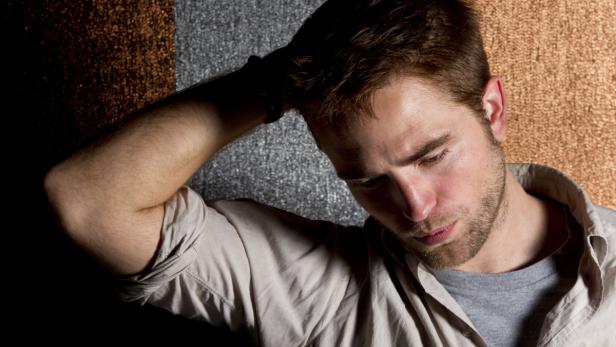 Robert Pattinson posiert vor einem strukturierten Hintergrund.