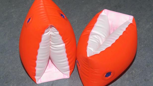 Zwei orangefarbene, aufblasbare Schwimmflügel liegen auf einem grauen Untergrund.