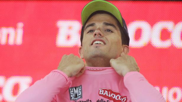 Ein Radrennfahrer im rosa Trikot und mit grüner Kappe feiert einen Sieg.