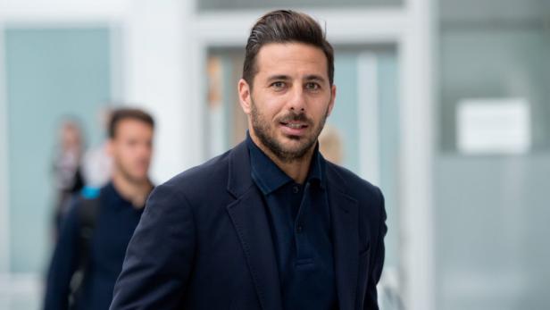 Ein Mann mit dunklem Haar und Bart trägt ein blaues Sakko.