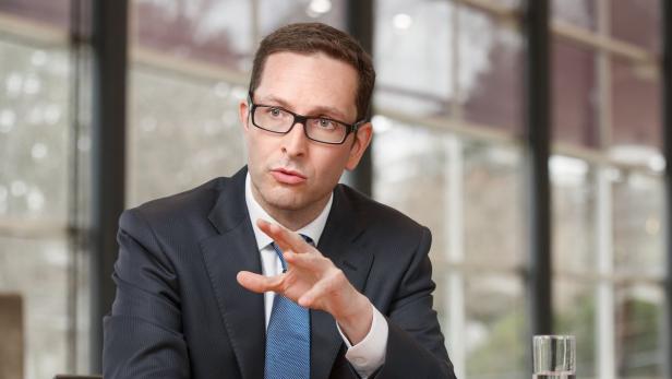 Ein Mann mit Brille, Anzug und Krawatte gestikuliert während eines Gesprächs.