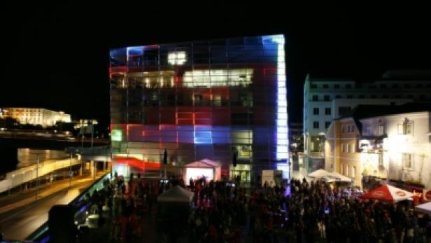 Eine Menschenmenge versammelt sich nachts vor einem modern beleuchteten Gebäude.