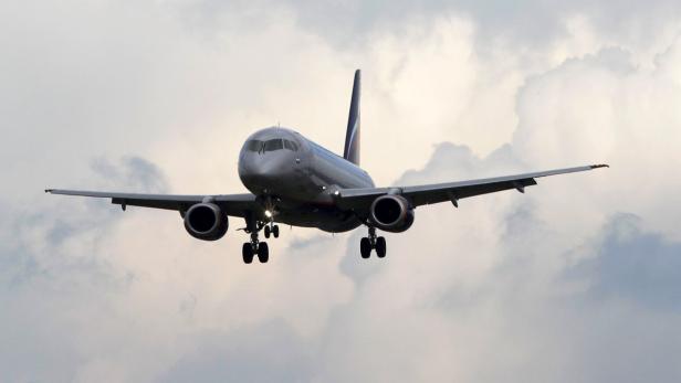Ein silbernes Passagierflugzeug landet vor einem bewölkten Himmel.