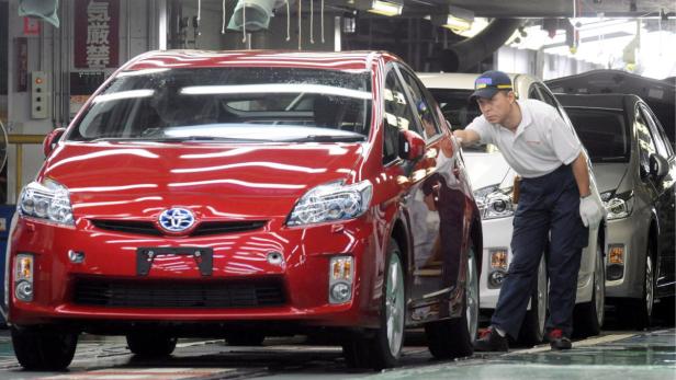 Ein Arbeiter inspiziert einen roten Toyota Prius in einer Fabrik.
