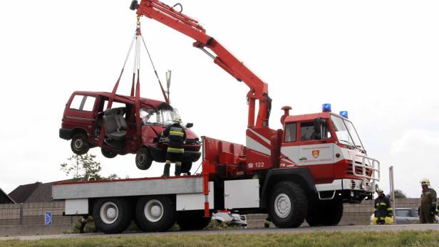 Ein Feuerwehrkran hebt ein rotes, beschädigtes Auto auf einen Lastwagen.