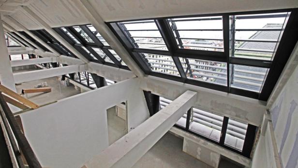 Innenansicht eines Rohbaus mit großen Dachfenstern und Blick auf die Stadt.
