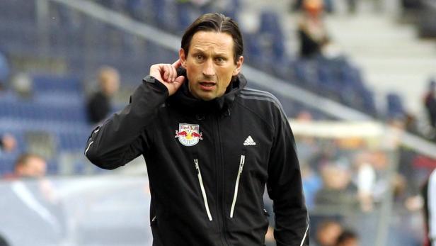 Ein Mann in einer schwarzen Jacke mit dem Red Bull Salzburg Logo am Kragen hält sich das Ohr zu.