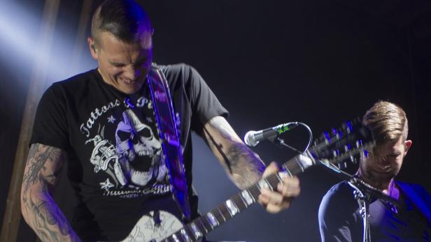 Ein Mann mit Tätowierungen spielt auf der Bühne Gitarre.