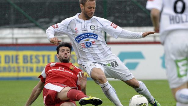 Ein Fußballspieler in Weiß dribbelt den Ball, während ein Gegenspieler in Rot zu Boden geht.