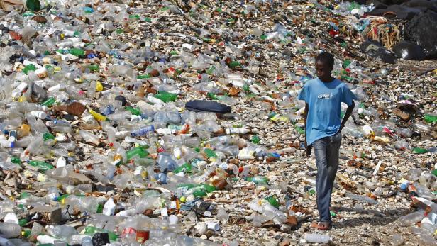 Ein Junge steht vor einem Berg aus Plastikmüll.