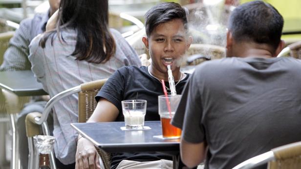 Ein junger Mann raucht eine E-Zigarette an einem Tisch im Freien.