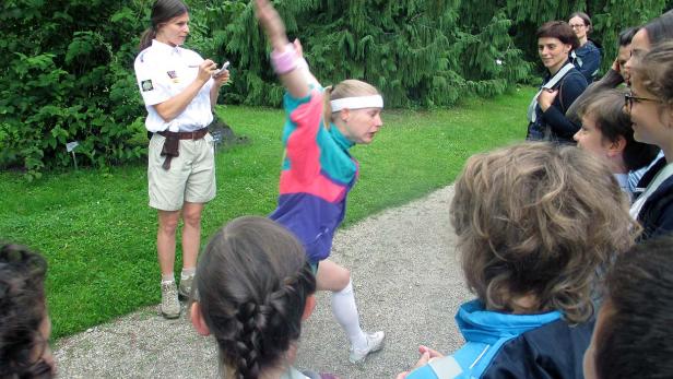Eine Frau in Sportkleidung führt eine Übung vor einer Gruppe von Zuschauern im Freien vor.