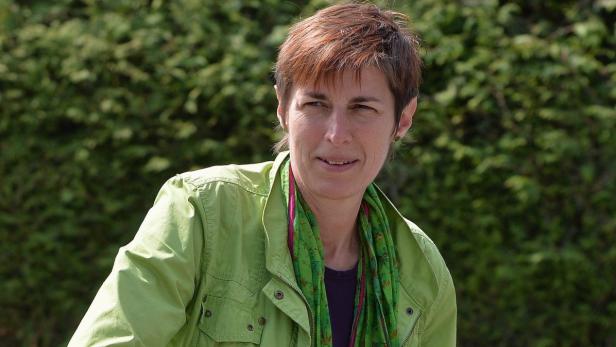 Eine Frau mit kurzem braunem Haar trägt eine grüne Jacke und einen bunten Schal.