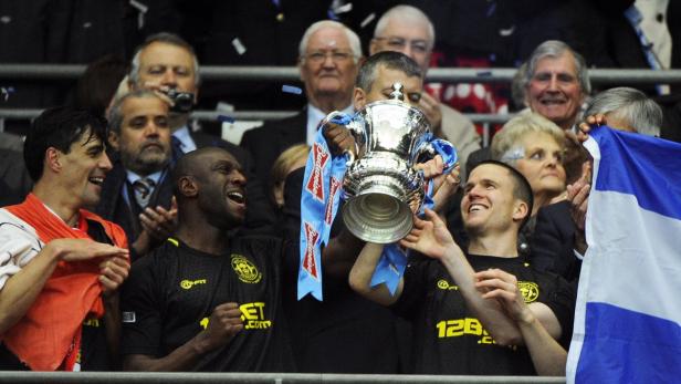 epa03696600 Wigan Athletic&#039;s (L-R) Paul Scharner, Emmerson Boyce and captain Gary Caldwell lift the trophy after winning the English FA Cup final soccer match between Manchester City and Wigan Athletic at Wembley in London, Britain, 11 May 2013. EPA/ANDY RAIN DataCo terms and conditions apply. https://www.epa.eu/downloads/DataCo-TCs.pdf
