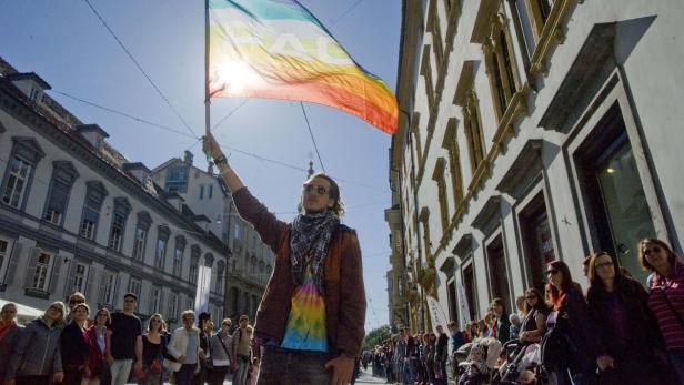 Ein Mann hält eine Regenbogenflagge mit der Aufschrift „Peace“ bei einer Demonstration in die Höhe.