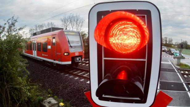 Ein roter Zug der Deutschen Bahn steht vor einem geschlossenen Bahnübergang.
