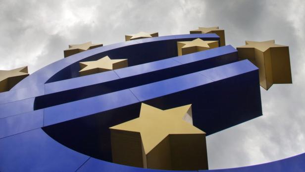 Eine blaue Euro-Skulptur mit goldenen Sternen vor einem bewölkten Himmel.