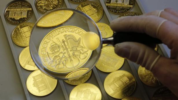 Eine Hand mit Handschuh hält eine Lupe über eine Goldmünze der Wiener Philharmoniker.