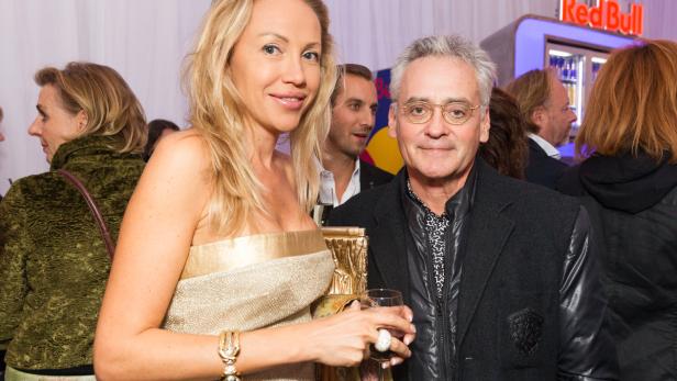 Eine Frau in einem goldenen Kleid und ein Mann mit Brille posieren für ein Foto.