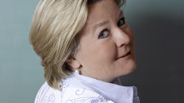 Eine Frau mit blonden Haaren und blauem Hemd blickt über ihre Schulter.