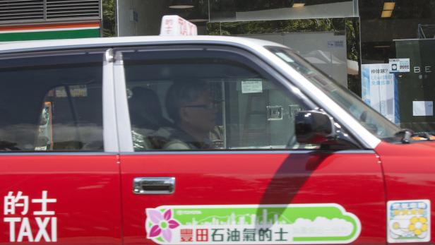 Ein rotes Taxi mit chinesischen Schriftzeichen und einem Fahrer in Hongkong.