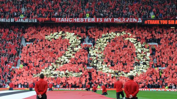 Volles Fußballstadion mit roter und goldener Choreografie und Bannern.