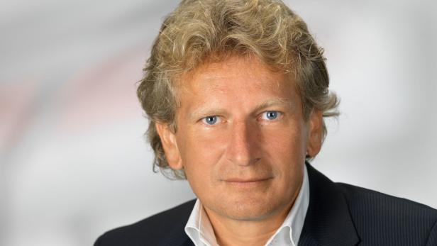 Porträt eines Mannes mit blonden, gewellten Haaren und blauen Augen.