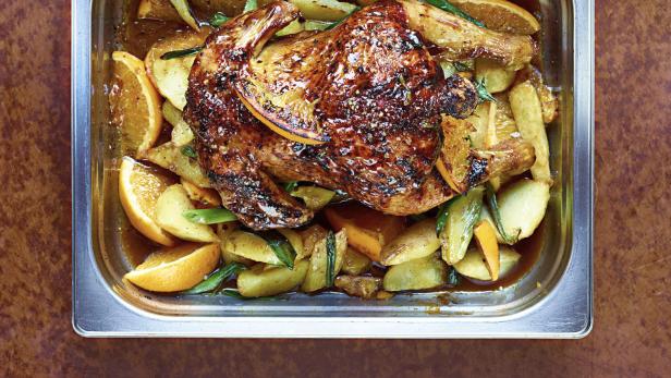 Ein Brathähnchen mit Kartoffeln und Orangenscheiben in einer Metallform.