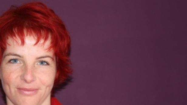 Eine Frau mit roten Haaren und einem roten Blazer lächelt.