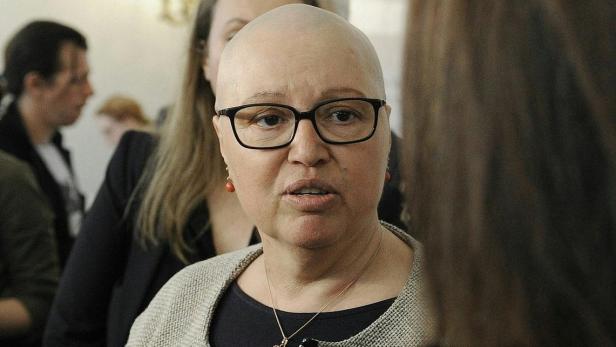 Eine Frau mit Brille und kurzem Haar spricht mit jemandem im Vordergrund.