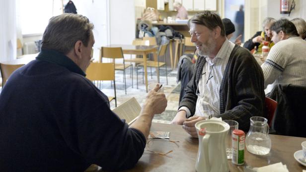 Zwei Männer sitzen an einem Tisch und unterhalten sich bei Kaffee.