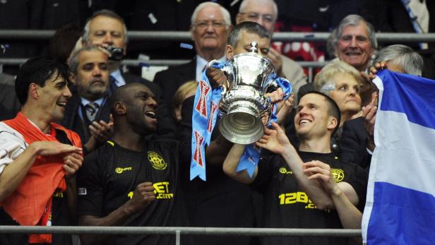 epa03696600 Wigan Athletic&#039;s (L-R) Paul Scharner, Emmerson Boyce and captain Gary Caldwell lift the trophy after winning the English FA Cup final soccer match between Manchester City and Wigan Athletic at Wembley in London, Britain, 11 May 2013. EPA/ANDY RAIN DataCo terms and conditions apply. https://www.epa.eu/downloads/DataCo-TCs.pdf