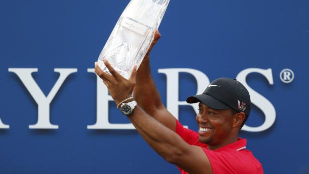 Tiger Woods hält eine Trophäe in die Höhe und lächelt.