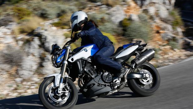 Eine Frau fährt mit einem BMW F 800 R Motorrad auf einer kurvigen Straße.
