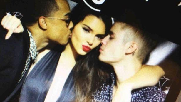 Kendall Jenner wird von zwei Männern auf die Wange geküsst.