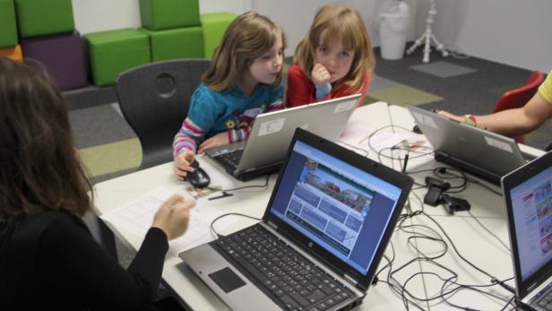 Zwei Mädchen sitzen an einem Tisch und arbeiten an ihren Laptops.