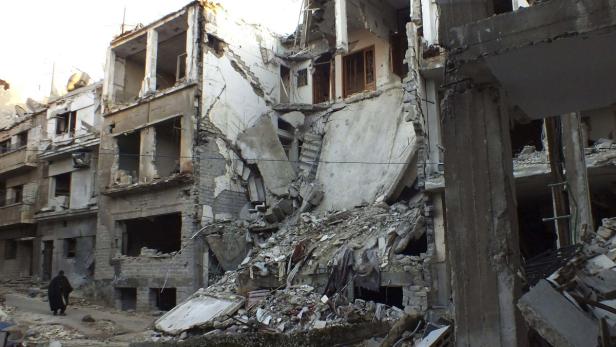 A man walks along a street lined with damaged buil