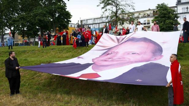 Eine Gruppe von Menschen hält ein großes Banner mit einem verzerrten Porträt von Recep Tayyip Erdoğan.