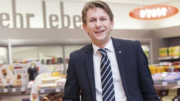 Ein Mann im Anzug steht in einem Supermarkt vor Regalen mit Lebensmitteln.