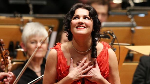 Eine Opernsängerin in einem roten Kleid singt vor einem Orchester.