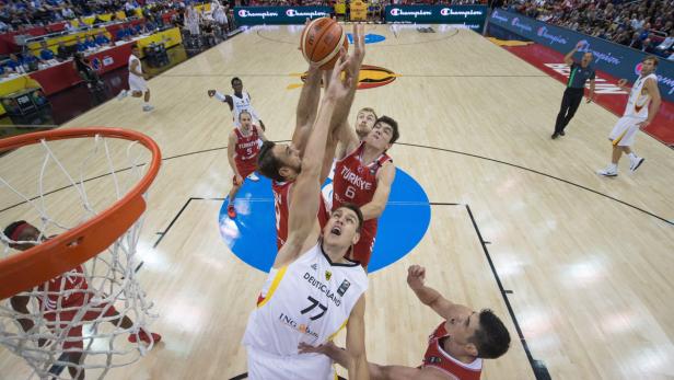Ein Basketballspieler Deutschlands versucht, den Ball gegen türkische Gegenspieler zu verteidigen.