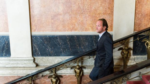 Ein Mann in einem Anzug steigt eine Treppe mit goldenen Engelstatuen hinauf.