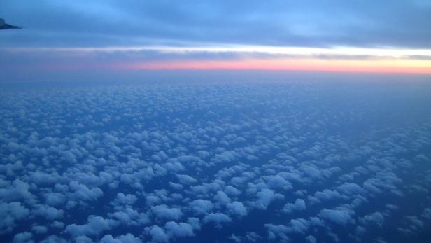Blick aus einem Flugzeug auf eine Wolkendecke bei Sonnenaufgang.