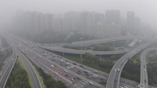 Eine mehrspurige Autobahn mit viel Verkehr führt durch eine Stadt im Nebel.