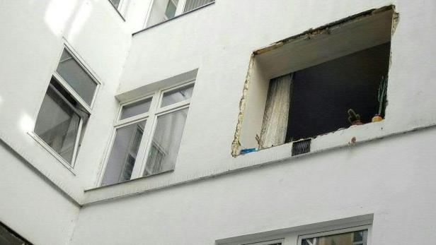 Die Fassade eines Hauses mit einem zerstörten Fenster, in dem ein Kaktus steht.
