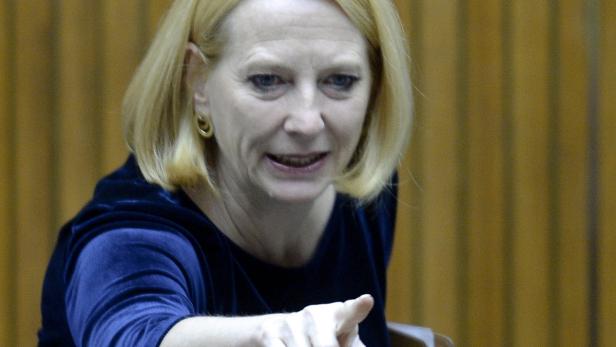 Eine Frau mit blonden Haaren und blauem Samtkleid zeigt mit dem Finger.