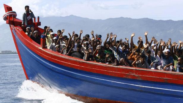 Ein überfülltes Boot mit Menschen an Bord fährt auf dem Wasser und die Menschen winken.
