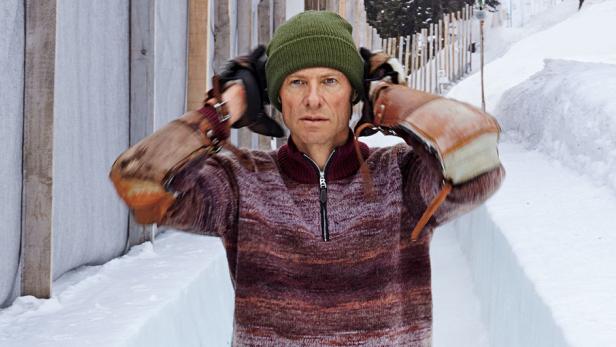 Ein Mann mit Mütze und alten Eishockeyhandschuhen steht im Schnee.