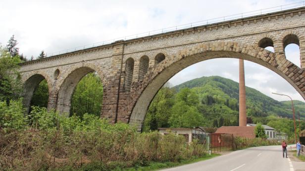 Eine Steinbogenbrücke überspannt eine Straße in ländlicher Umgebung.