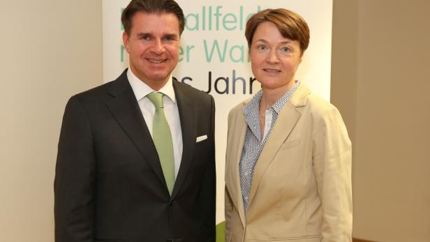 Ein Mann im Anzug und eine Frau im Blazer stehen nebeneinander vor einem Banner.